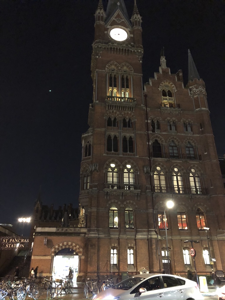 Clock towner with attached to grand old building with sloping roofs. Night time view. It looks like the Houses of Parliament.