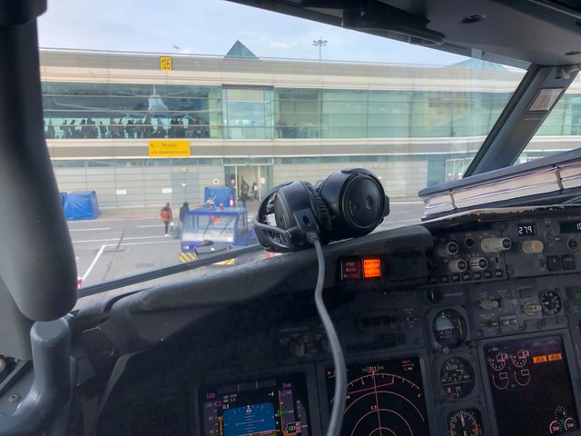 Cockpit of an airplane. Some headset headphones sit on the dashboard. The terminal can be seen through the window.