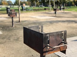 BBQ area with sandy gravel ground. At least three permanent barbeques can be seen.
