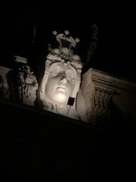 A stone carved head on a building, lit up in the dark