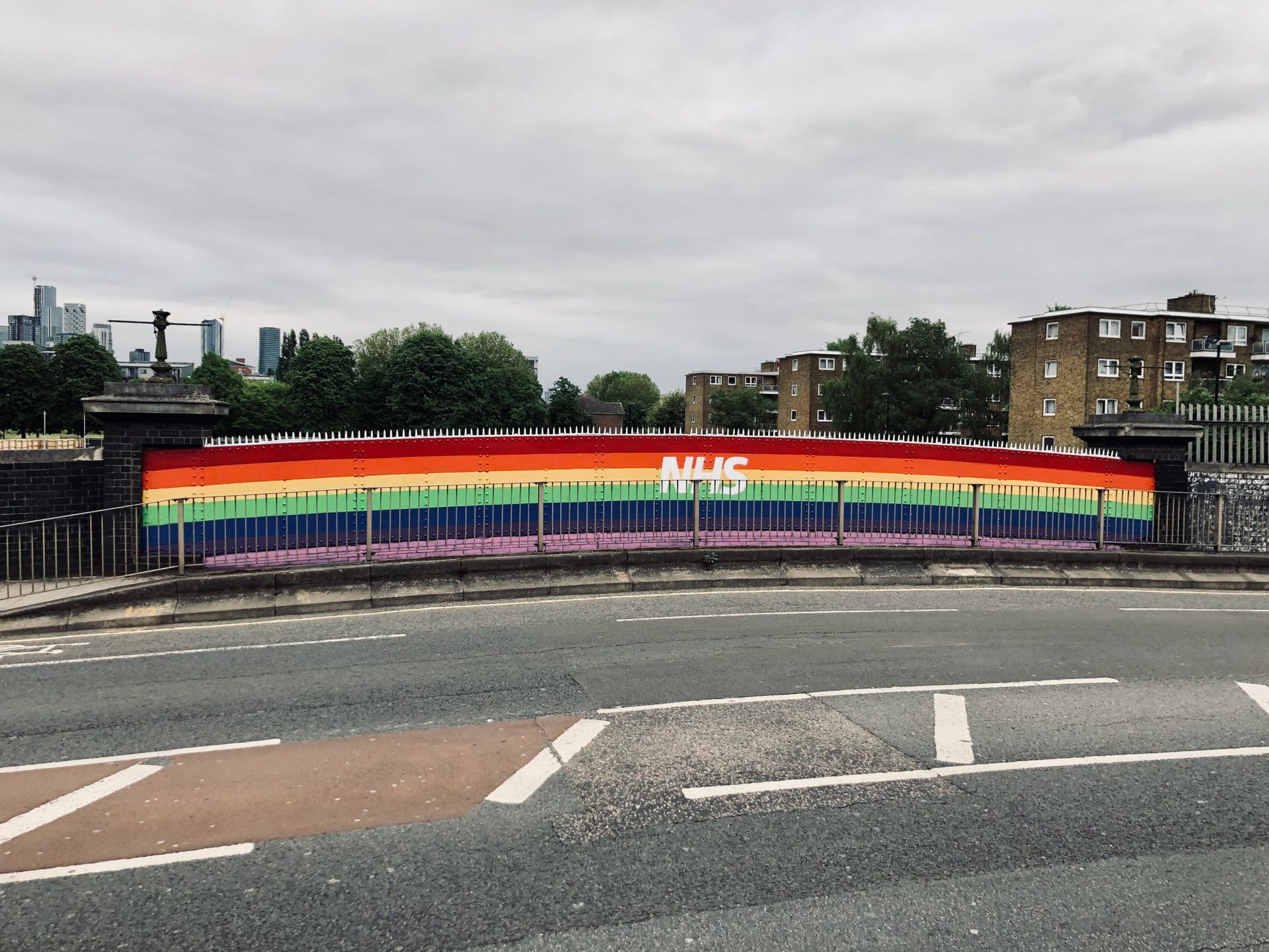 Rainbow painting with word NHS in white over it on wall of Blackhorse Bridge by the pavement and road
