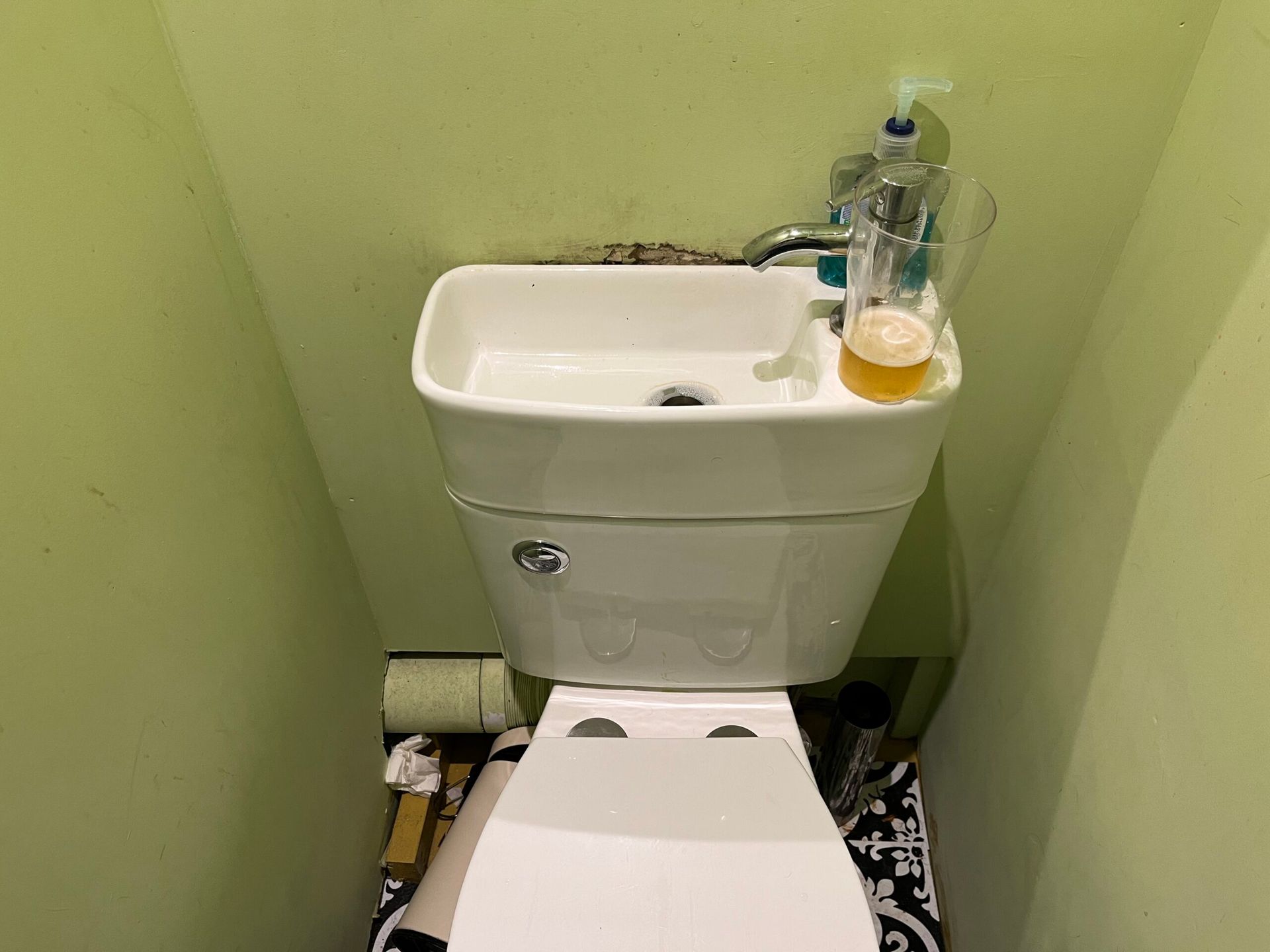 Toilet with a sink in the cistern saving space. In a lime green cubical