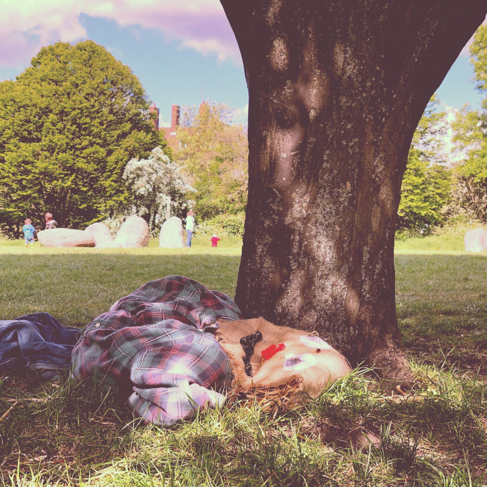 Straw man scarecrow lying under a tree looking dead. Stone circle in the background.